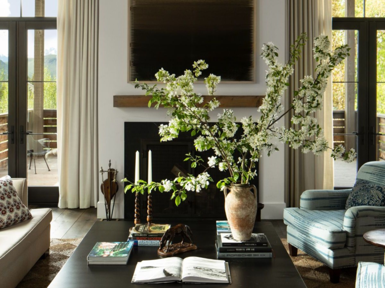 Spring living room with layered materials including linen curtains, wood accents, floral branches, and textured upholstery.